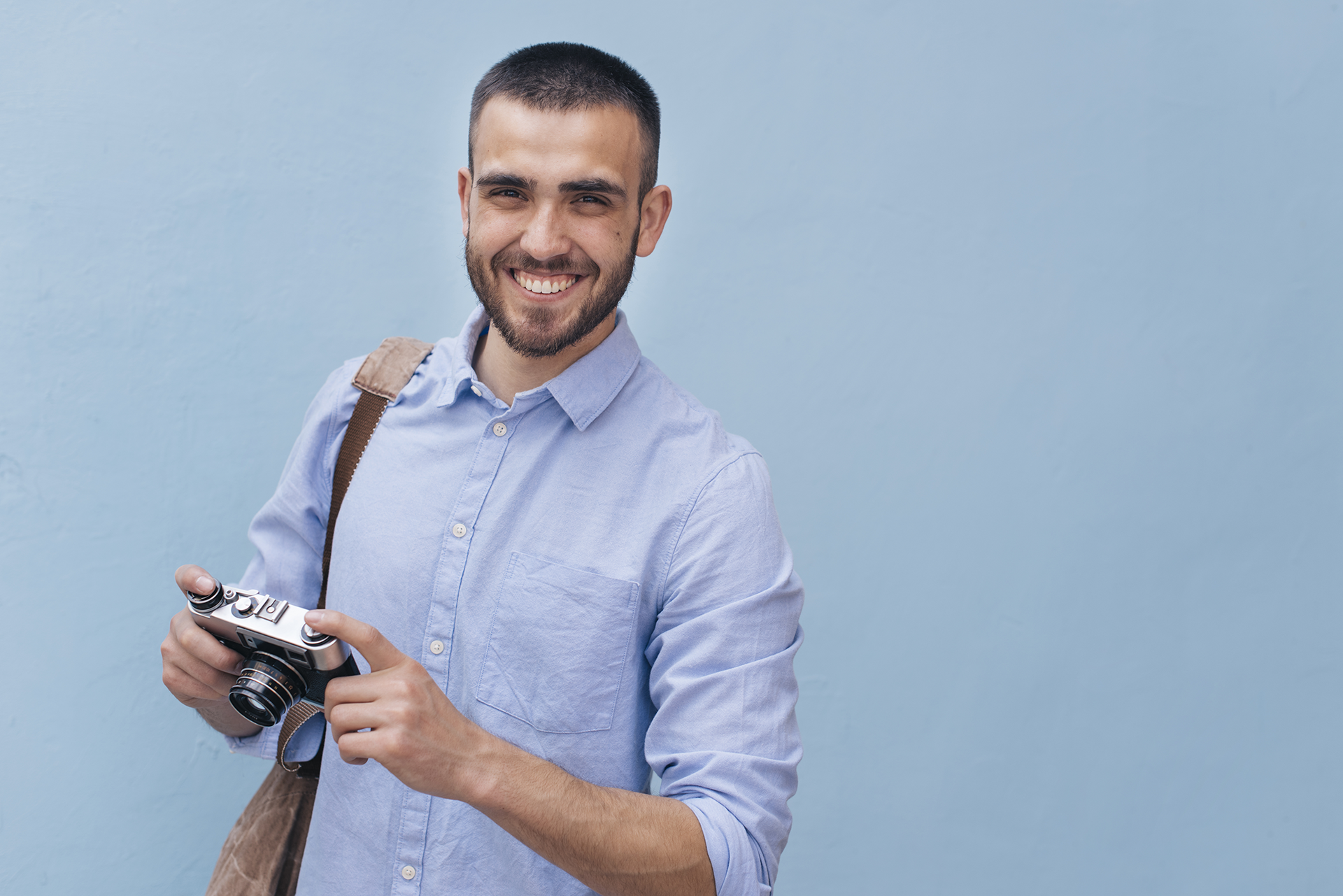 ©BCT-Business-und-Portraetfotograf_business_portrait-young-smiling-man-holding-camera-standing-against-blue-wall ©BCT-Business-und-Portraetfotograf_business_portrait-young-smiling-man-holding-camera-standing-against-blue-wall